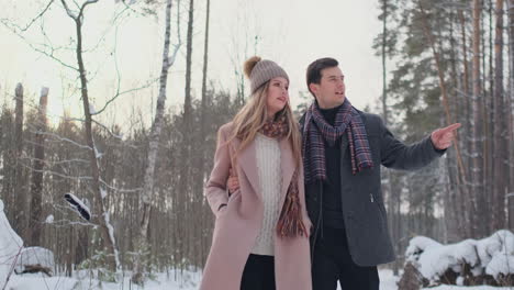 Young-married-couple-walks-through-the-winter-forest.-A-man-and-a-woman-look-at-each-other-laughing-and-smiling-in-slow-motion.